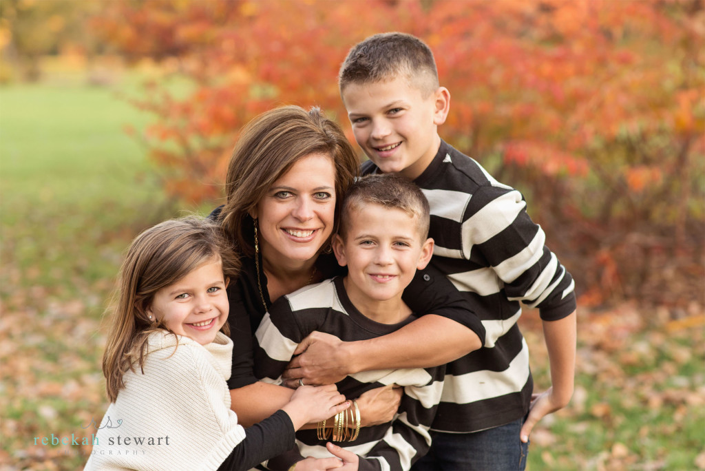 A mom and her kids snuggle in front of fall foliage | child