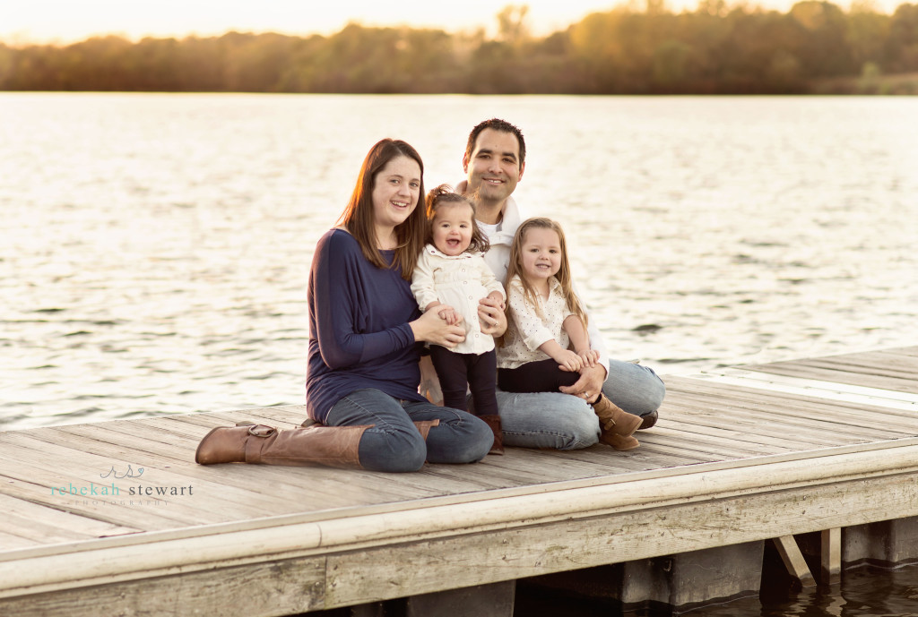 A beautiful family sits on a dock on a lake in the fall