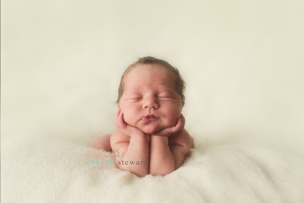 A baby girl is in head on hands pose on a blanket