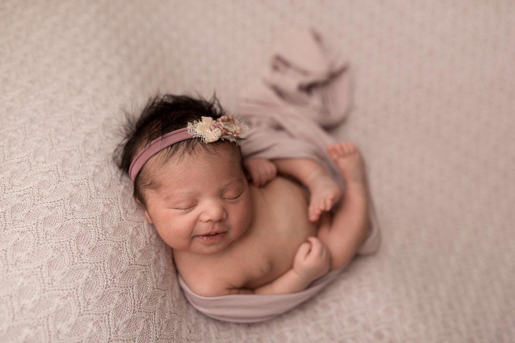 During her Cedar Rapids newborn photos, a baby girl on a purple blanket smiles, birth plan