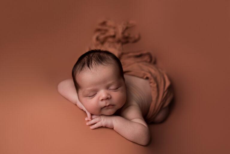A newborn baby boy sleeps on an orange blanket during his photography session in Cedar Rapids Iowa